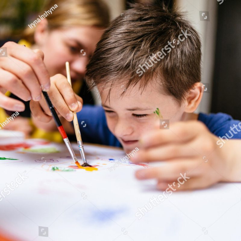 stock-photo-young-female-teacher-explain-talk-at-desk-with-a-down-syndrome-schoolboy-color-painting-for-2017134890